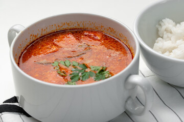Bowl of curry with pieces of meat and a side of steamed rice arranged neatly for a meal