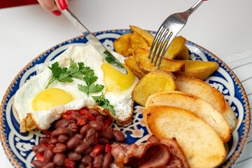 Woman enjoying a hearty breakfast with eggs, beans, and potatoes on a decorated plate at a dining table