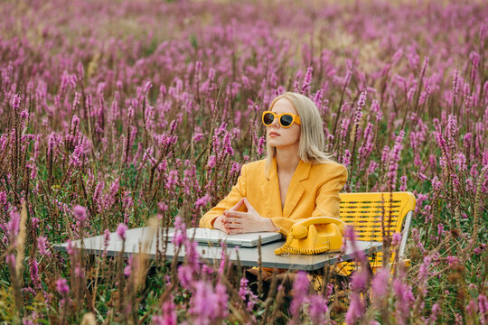 Thoughtful woman sitting near table with laptop and rotary phone in meadow