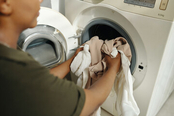 Person is loading clothes into a front-loading washing machine with a focus on hand placing...