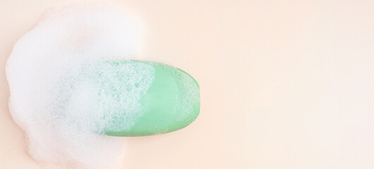 Fototapeta premium Top view of single antibacterial hygienic organic soap bar of green colour wet soapy and covered with foam bubbles laying on beige background with copy space used as toiletries at bath for skin care