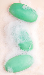 Fototapeta premium Top view of three hygienic antibacterial handmade soap bars of green colour wet soapy and covered with foam bubbles laying on beige background used as cosmetics or toiletries for skin and body care