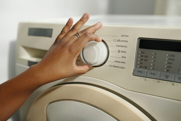 Close-up view of person adjusting settings on a front-loading washing machine. Display showing various fabric options with hand turning dial