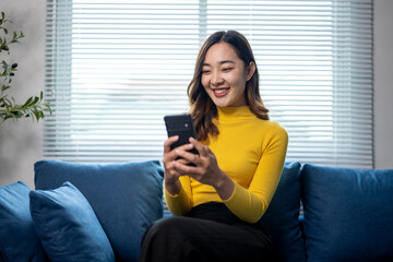 Happy young woman is using smartphone sitting on sofa at home