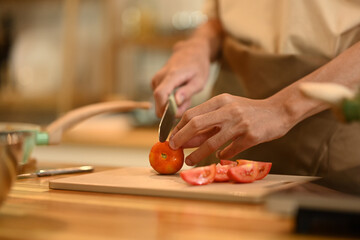 Close up image of man cutting tomatoes on a wooden cutting board, preparing healthy meal in kitchen