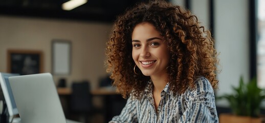 Portrait of a Happy Middle Eastern Manager Sitting at a Desk in Creative Office. Young Stylish Female with Curly Hair Using Laptop Computer in Marketing Agency