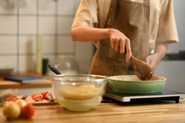 Close up of man using a spatula to stir and cook the ingredients in frying pan on an induction stove