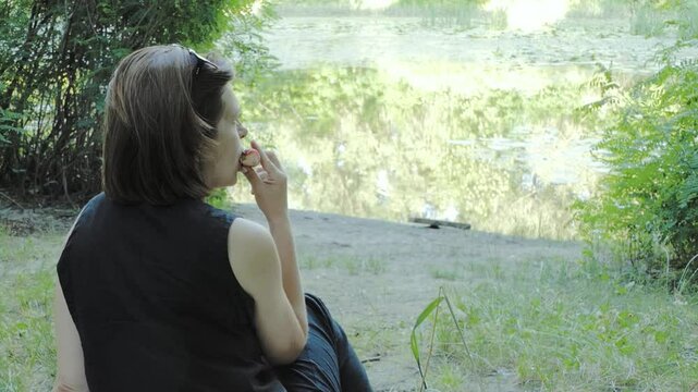 A woman eats a fig peach in a park during a picnic