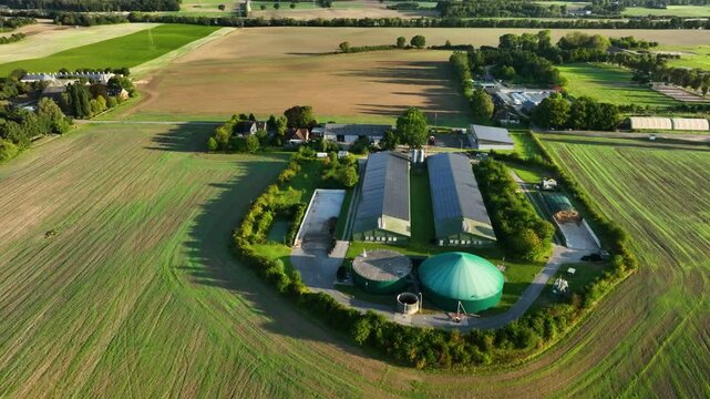 Retreating shot of biogas plant with photovoltaic panels on the roofs of barns. High-tech farming and renewable resources. Aerial footage of countryside with biogas plant and silo.