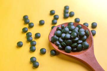 Closeup of Green biotin tablets on a brown wood spoon kept on a yellow background