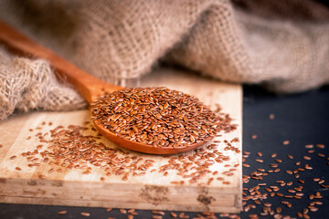 Side angle of healthy flax seeds scattered on a wooden spoon kept on the chopping board with a dark background 