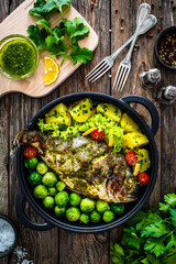 Roasted sea bream, boiled potatoes and brussels sprouts served in black dish on wooden table 