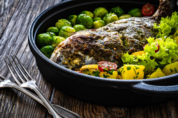 Roasted sea bream, boiled potatoes and brussels sprouts served in black dish on wooden table 