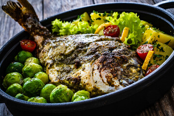 Roasted sea bream, boiled potatoes and brussels sprouts served in black dish on wooden table 