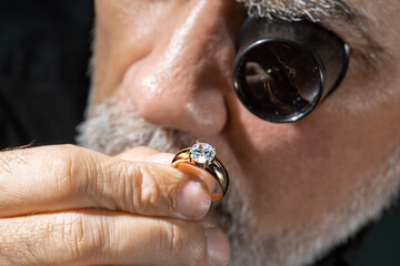 Jewelry appraiser examines a gold ring evaluating large diamond looking through magnifying glass...