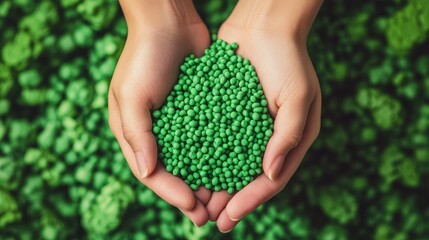 Close-up of hands holding a heap of green, eco-friendly biodegradable plastic pellets