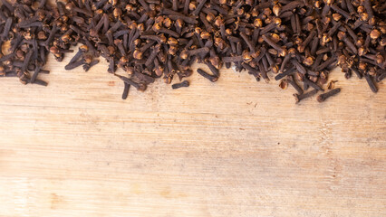 A spice of dried cloves lies on a wooden spoon and is scattered on old wooden boards. And a space for text.