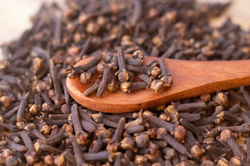 A close-up image of a pile of dried cloves on a wooden spoon. The cloves are a dark brown color and have a distinct, knobby shape. They are clustered together, showing their intricate textures