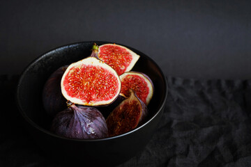 Ripe whole and sliced ​​figs in a black plate on a dark background