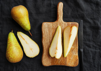 Ripe sliced ​​and whole pears on a wooden board next to a knife on a dark background