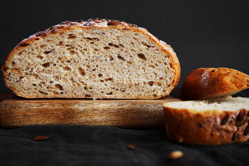 Fresh grain bread next to cut pieces on a wooden board on a dark background