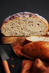 Fresh grain bread next to cut pieces on a wooden board on a dark background