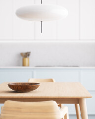 A modern minimalist kitchen with a wooden dining table and chic pendant light fixture