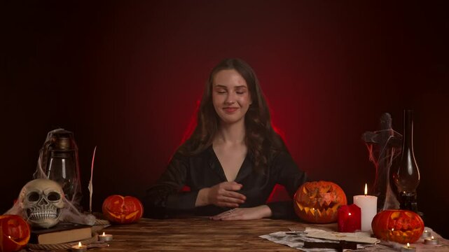 Halloween gothic woman witch fortune teller sitting at table shows ok good hand sign, smiling positive nodding head in acceptance. Magic halloween concept.