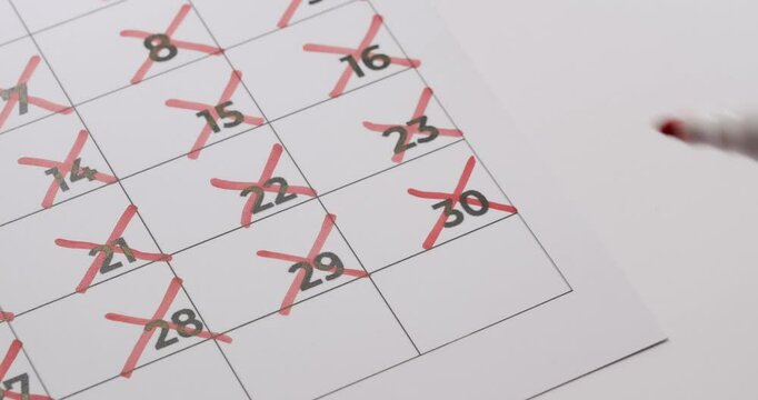 Close-up of a hand marking the last day of the month on a calendar with a red marker, indicating the passage of time and planning. Marking the Last Day of the Month on a Calendar with Red Marker