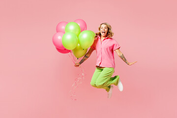 Full body young shocked surprised woman wear shirt celebrating birthday holiday stand hold bunch of colorful air balloons jump high isolated on plain pastel light pink background. Lifestyle concept.
