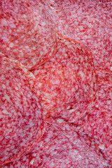 Close-up of thinly sliced salami arranged in overlapping layers. The rich red texture and marbled fat create an appetizing, detailed view perfect for culinary or food-related projects.