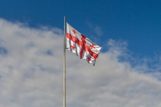 A large Georgian flag flutters against a cloudy sky.