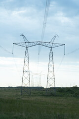 High voltage pylons against the blue sky with white clouds and bright green meadow. Power lines stretching into the distance. Perspective. Electricity