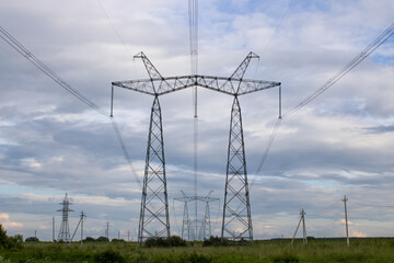 High voltage pylons against the blue sky with white clouds and bright green meadow. Power lines stretching into the distance. Perspective. Electricity