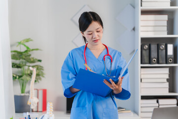 Focused and Compassionate: A female doctor in a blue medical scrubs, meticulously reviews patient...