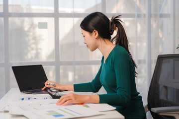 Focused on Finances: A young businesswoman meticulously analyzes financial data with a calculator...