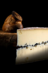 Slice of morbier french cheese with a loaf of crusty french bread on a black background