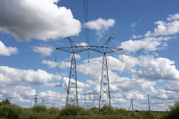 High voltage pylons against the blue sky with white clouds and bright green meadow. Power lines...