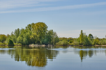 Serene landscape featuring calm water reflecting lush green trees along shoreline against blue sky