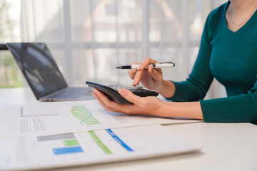 Focused on Finance: A woman meticulously works on financial reports, using a calculator and laptop....
