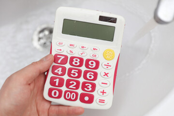 Obraz premium Hand holding calculator over the sink. Water consumption, savings