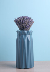 Dry lavender in vase on table, blue background