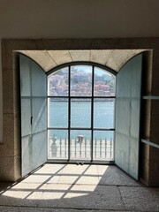 A serene glimpse of the Douro River at sunset, viewed through a window with light filtering in, casting a warm glow on the interior of a traditional building in Porto's port district.