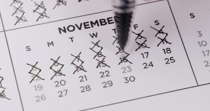 A person's hand uses a black pen to cross off days on a November calendar. They methodically mark each square with an 'X' as if counting down the days. Crossing Off Dates On November Calendar