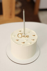 cake first birthday.white cake with the word one , with one candle on a white table . festive 
