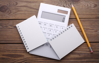 Two white blank spiral notebooks  with calculator and pencil on wooden background