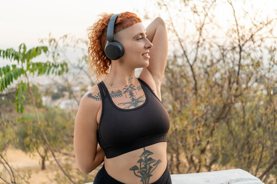 Slim woman in headphones stretching arms in park