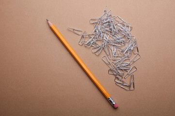 Metal paper clips and pencil on brown background