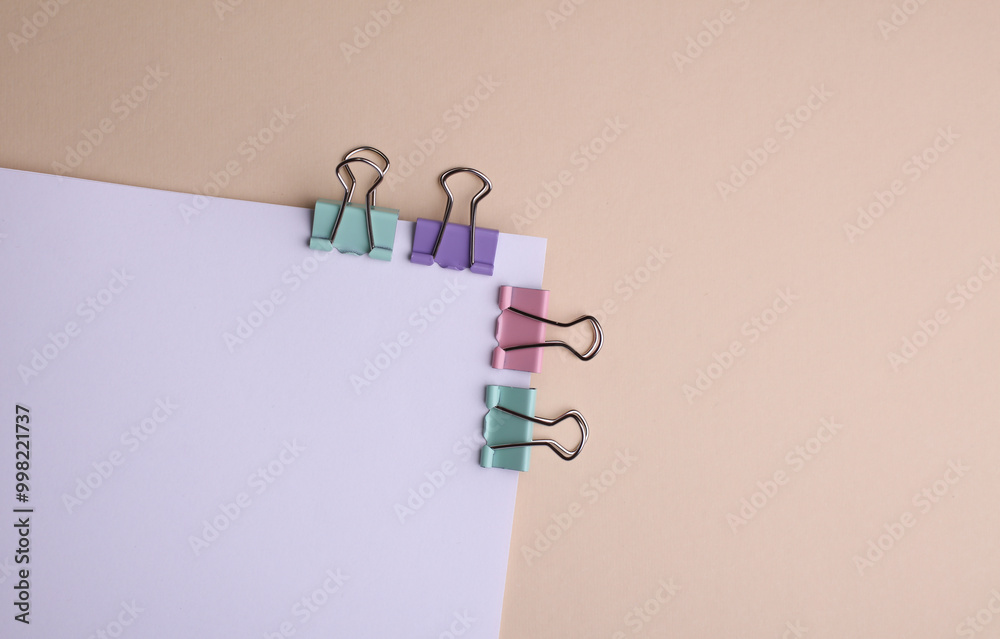 Wall mural white sheet of paper with colored binders on beige background