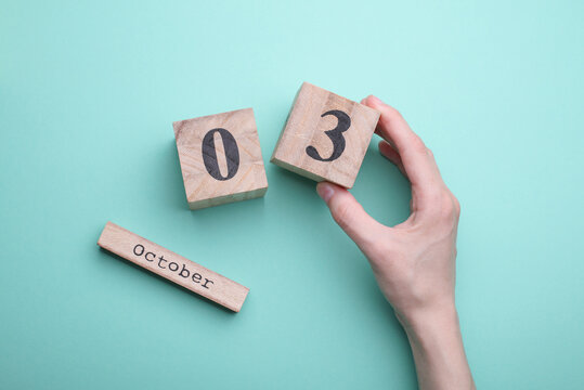 Hand holding wooden block calendar with date october 03 on mint green background